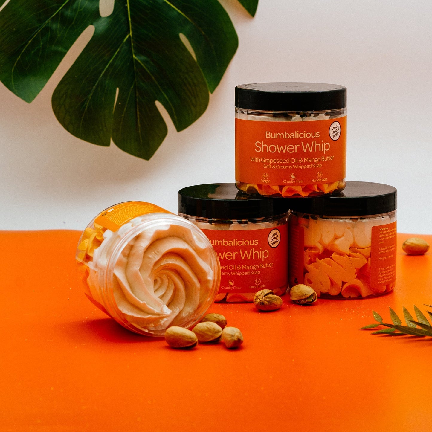 Bumbalicious Shower Whip jars on an orange surface with green leaves in the background